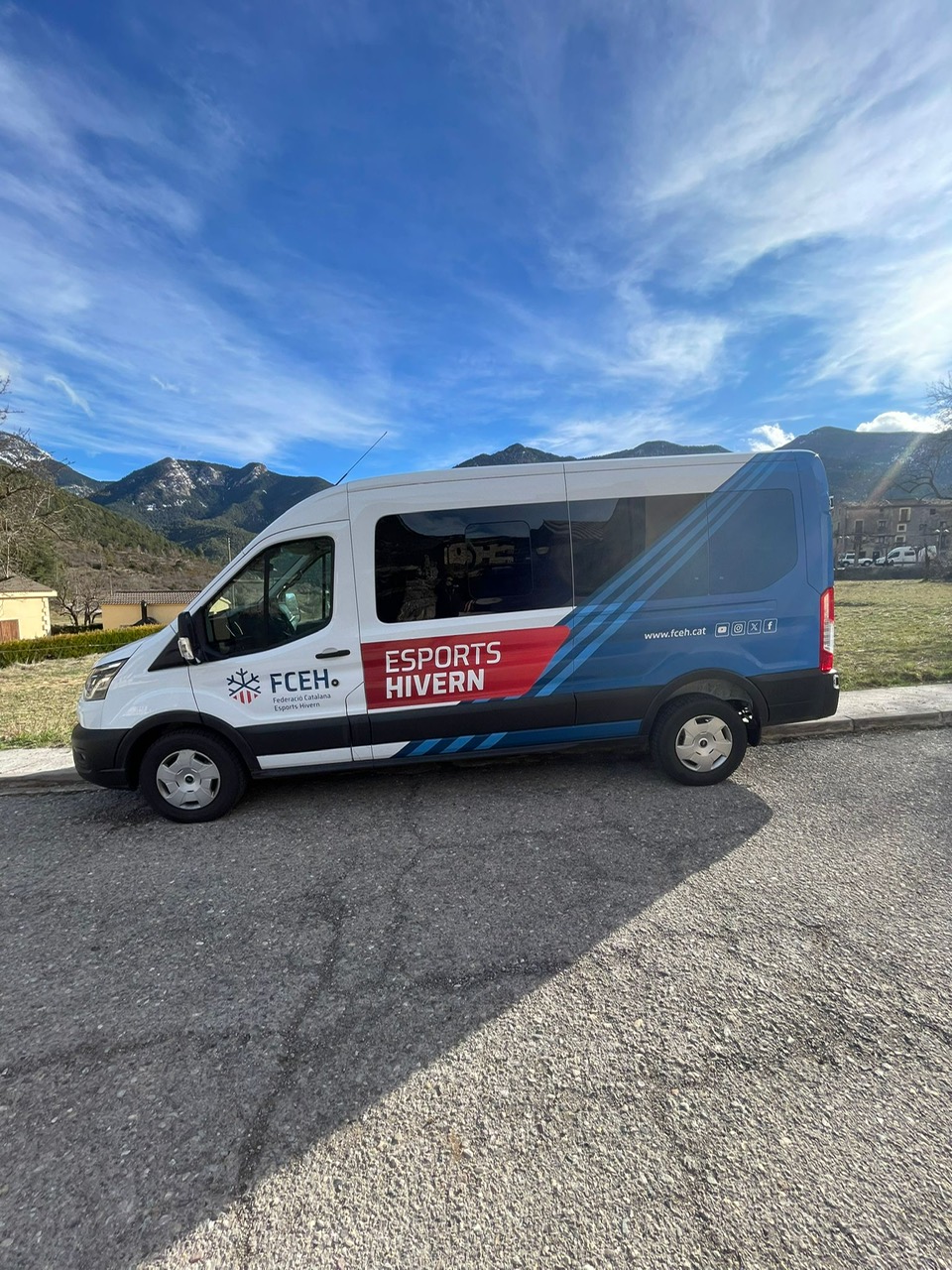 Vista lateral del Ford Transit oficial FCEH Esports Hivern con wrapping azul y rojo corporativo en paisaje de montaña